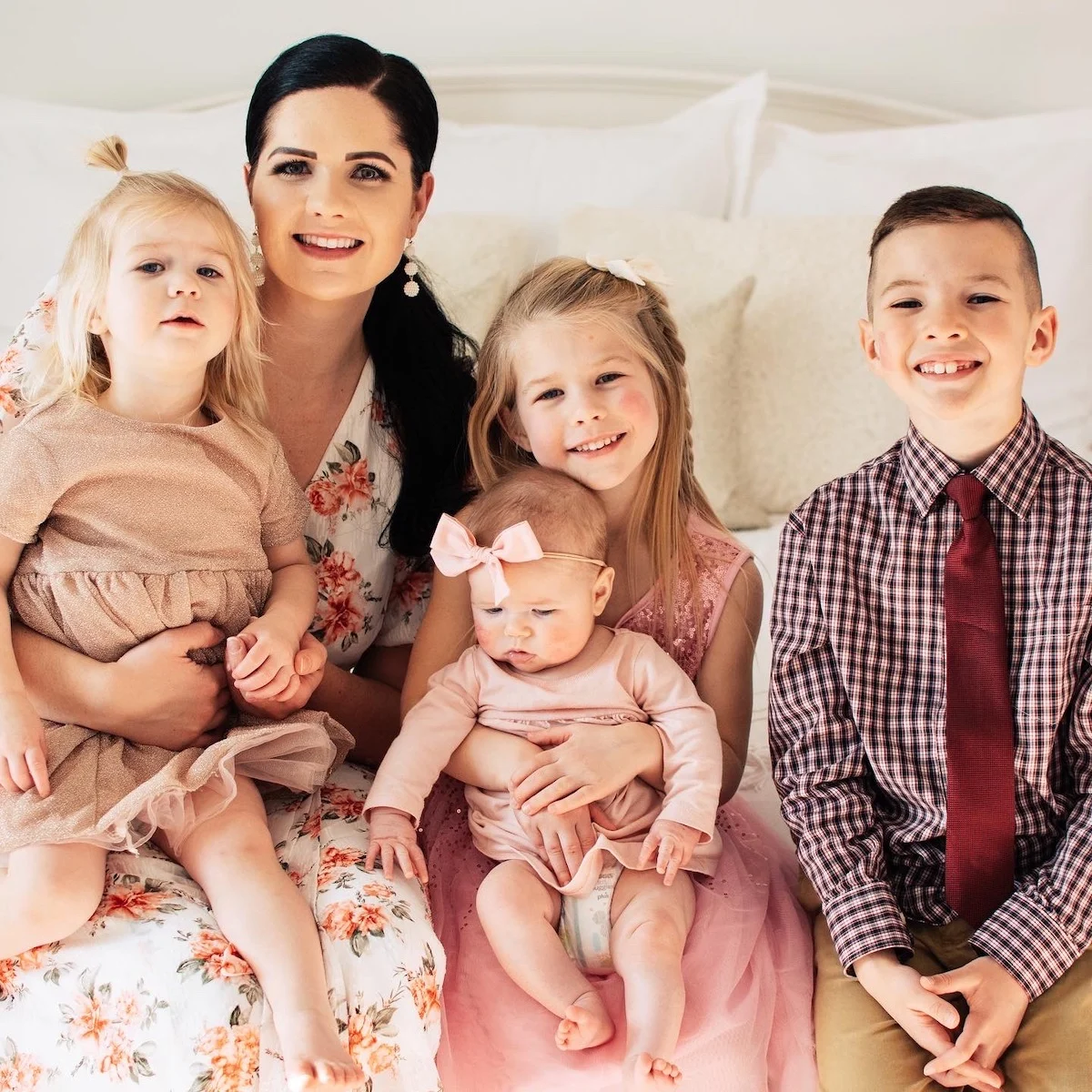 A mom poses with her children in coordinated outfits on a bed.