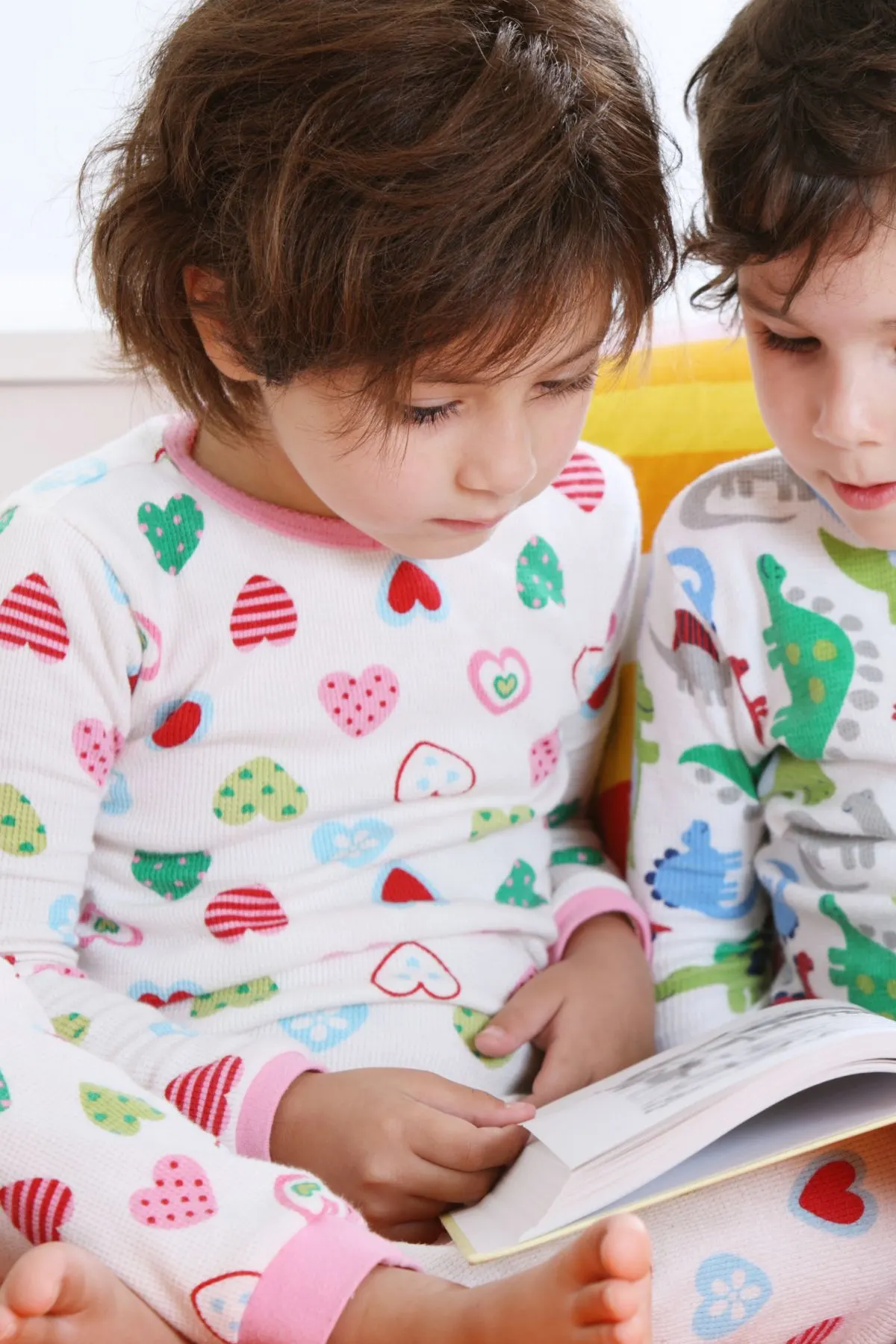 A boy and a girl read a book together in pajamas with hearts and dinosaurs.