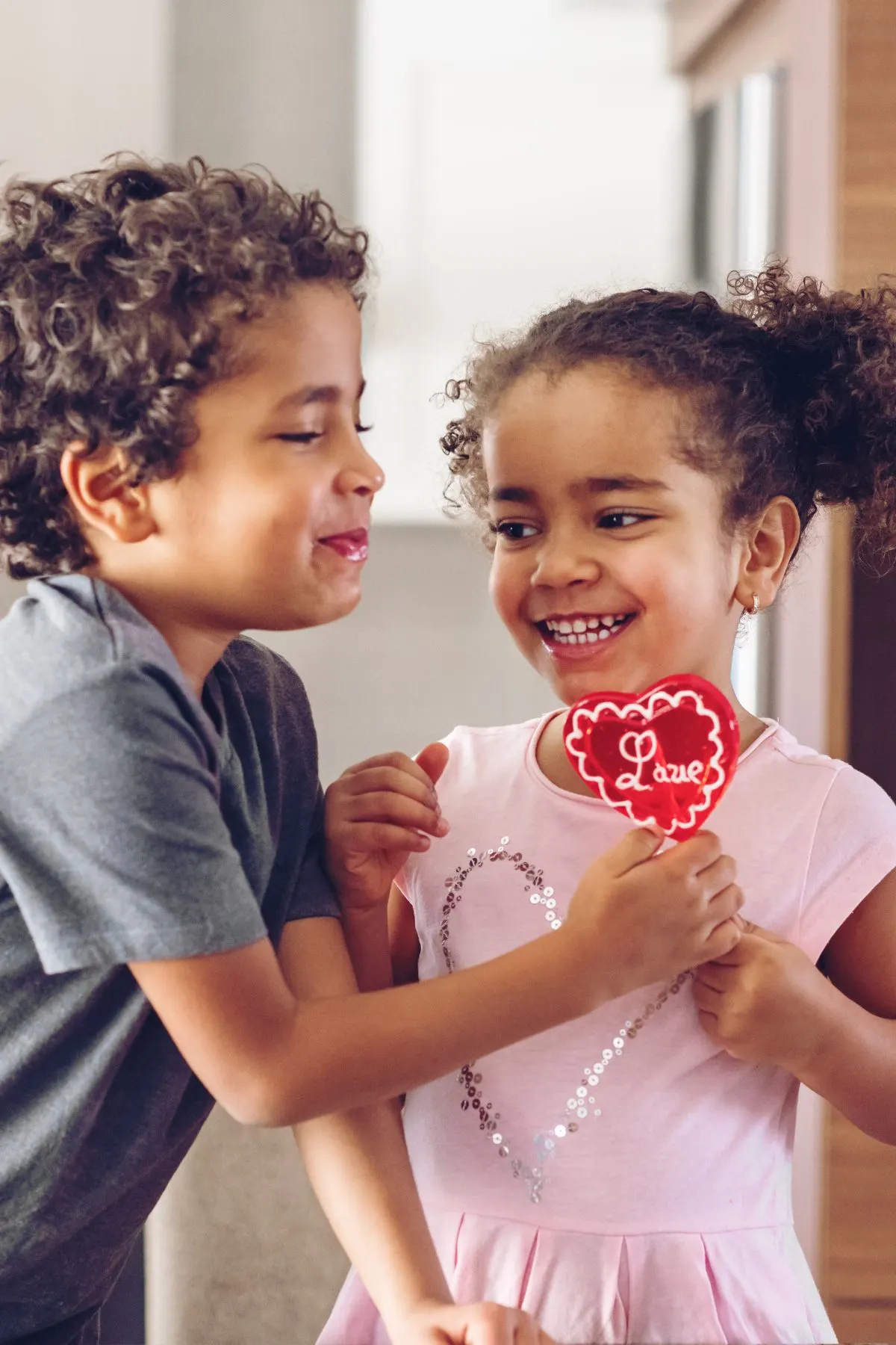 Smiling siblings hold a Valentine's Day sucker shaped like a heart.
