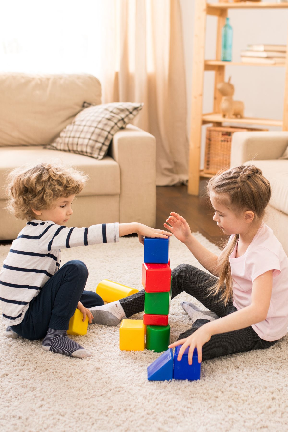Siblings build a tower out of blocks in a living room.