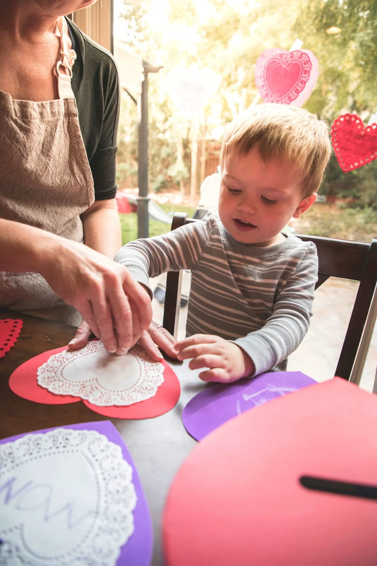 Toddler working on heart-shaped crafts for Valentine's Day with mom.