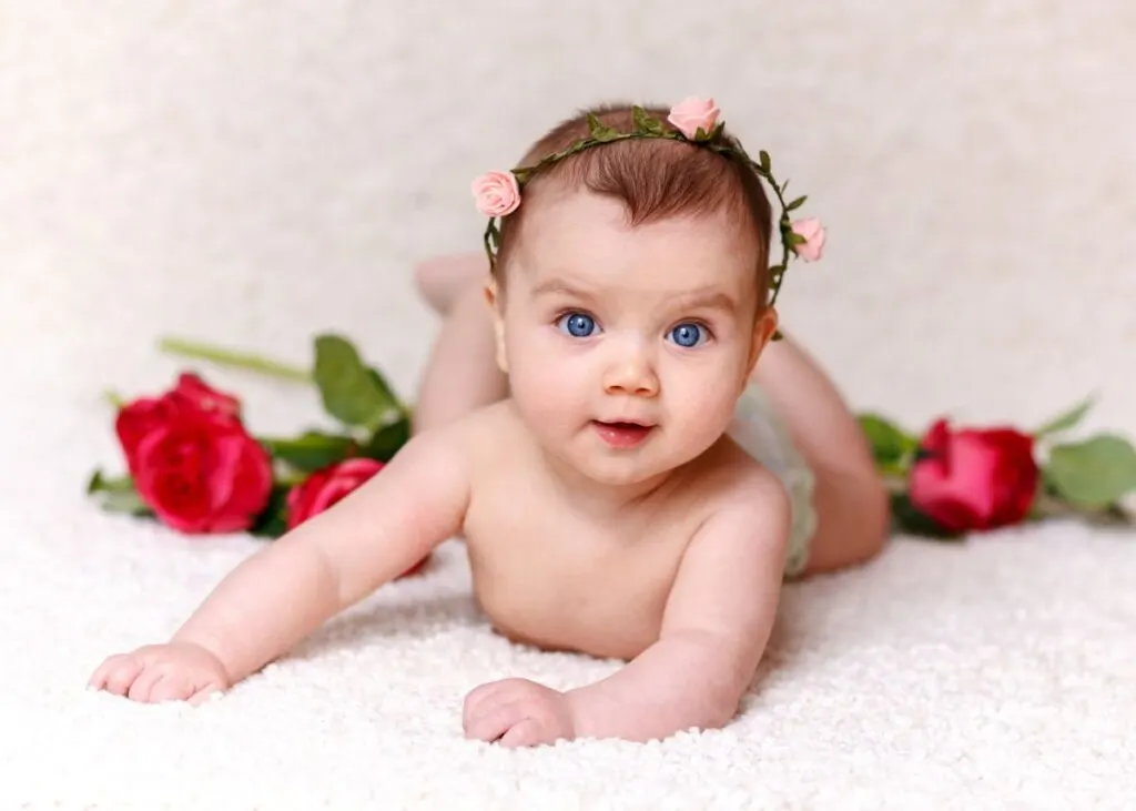 Baby girl with rose headband pushes up on tummy with red roses in background.