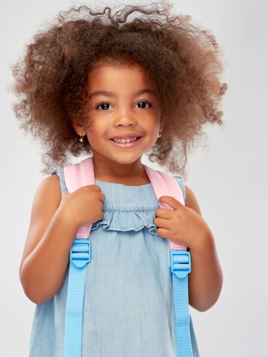 A girl with big curly hair and a pink and blue backpack.