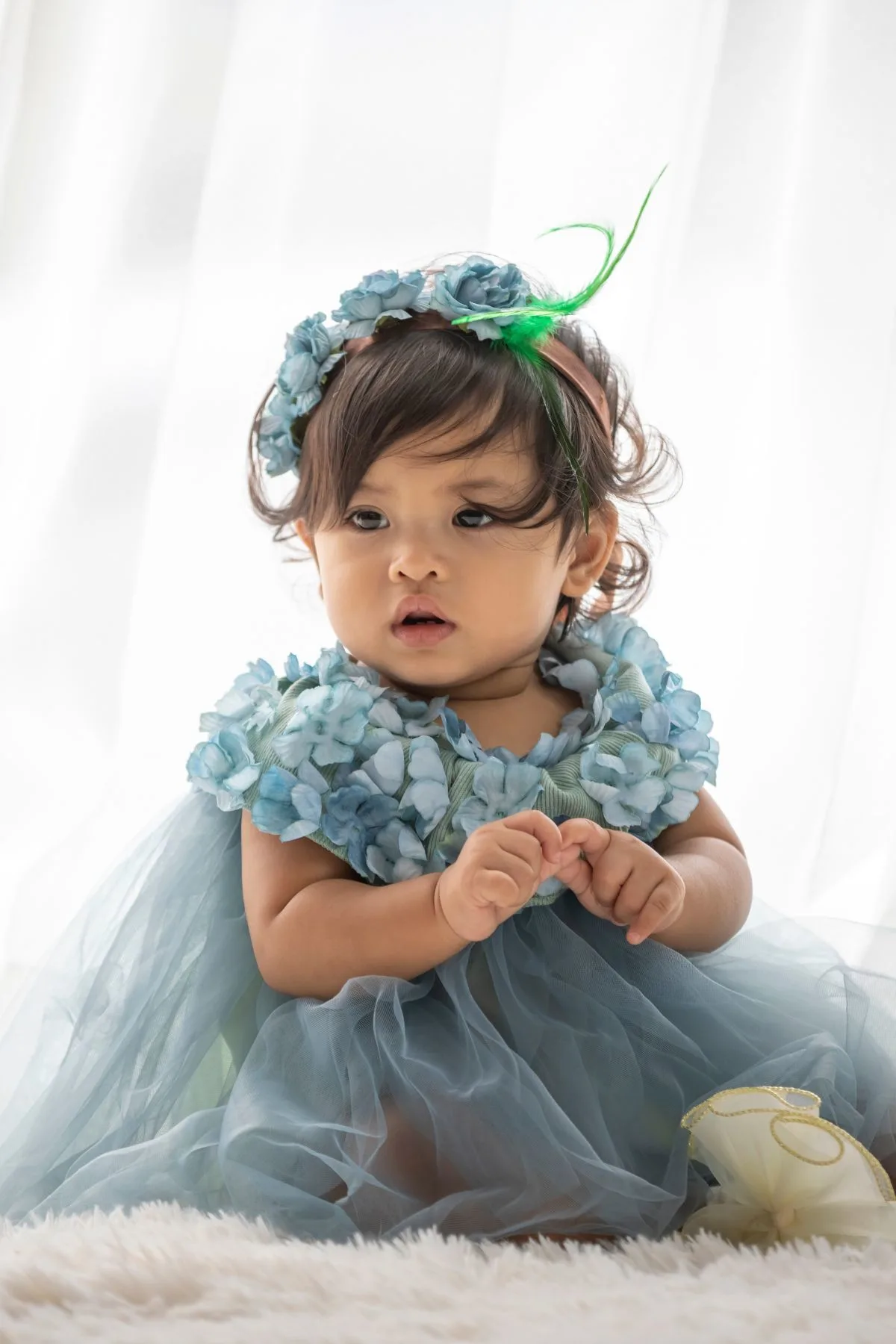 Baby girl in a blue dress and a blue and green flower crown.