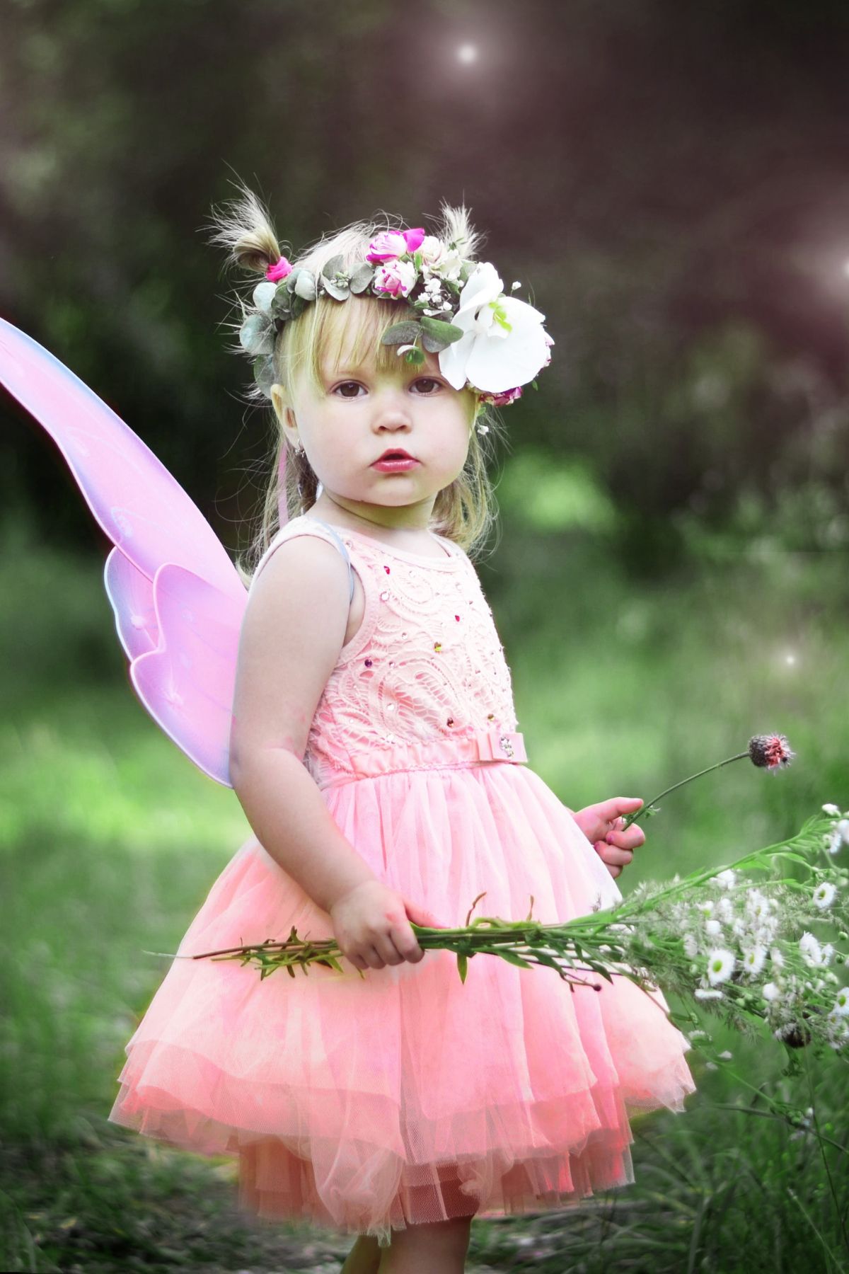 Little girl with flower crown, fairy wings, and flowers in the forest.