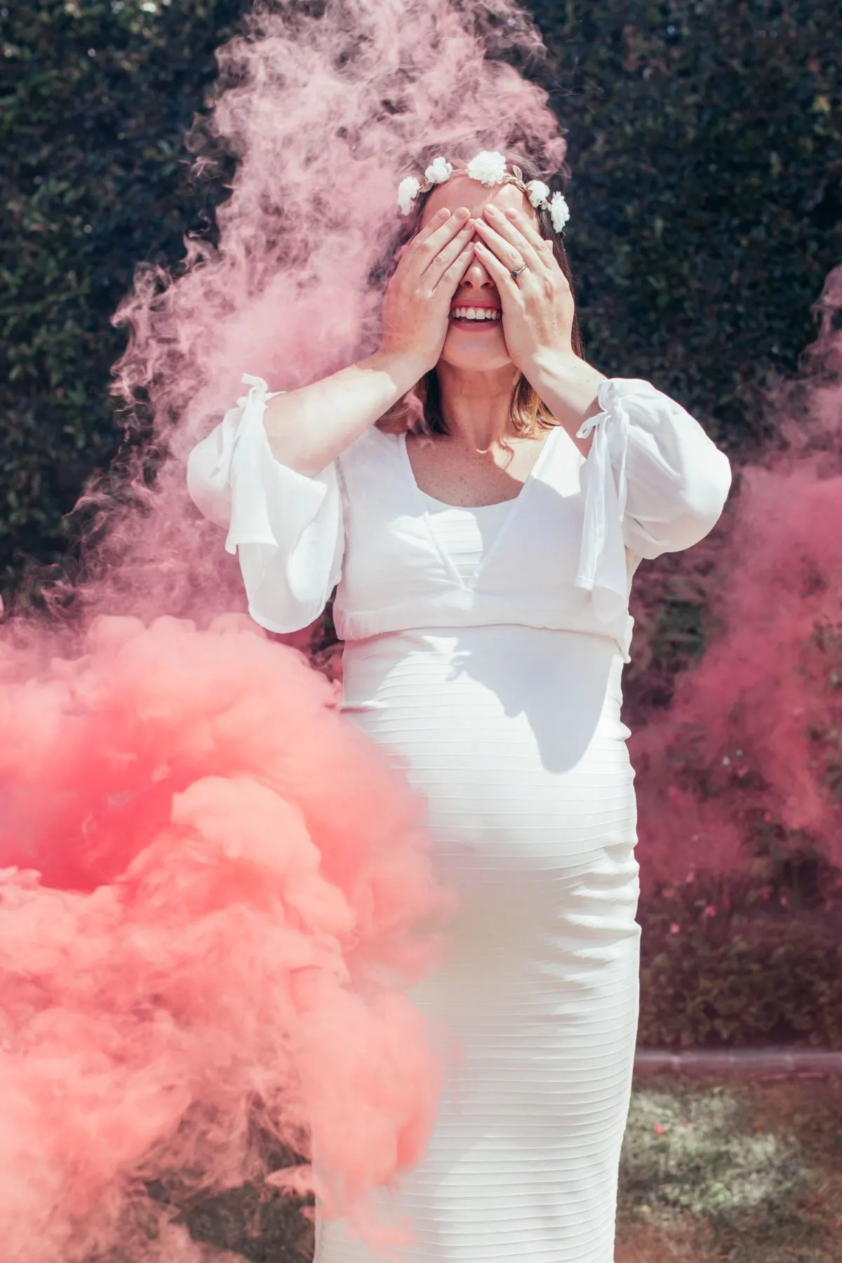 A woman in a white dress covers here eyes while surrounded by pink powder.