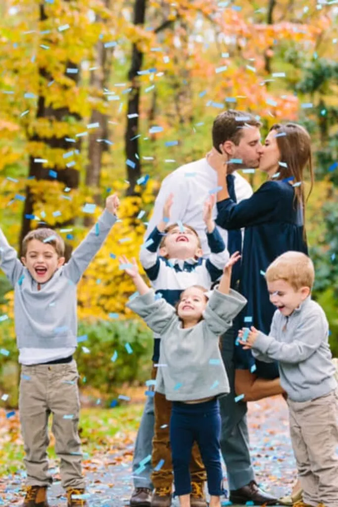 A couple kisses behind their children while blue confetti falls to the ground.