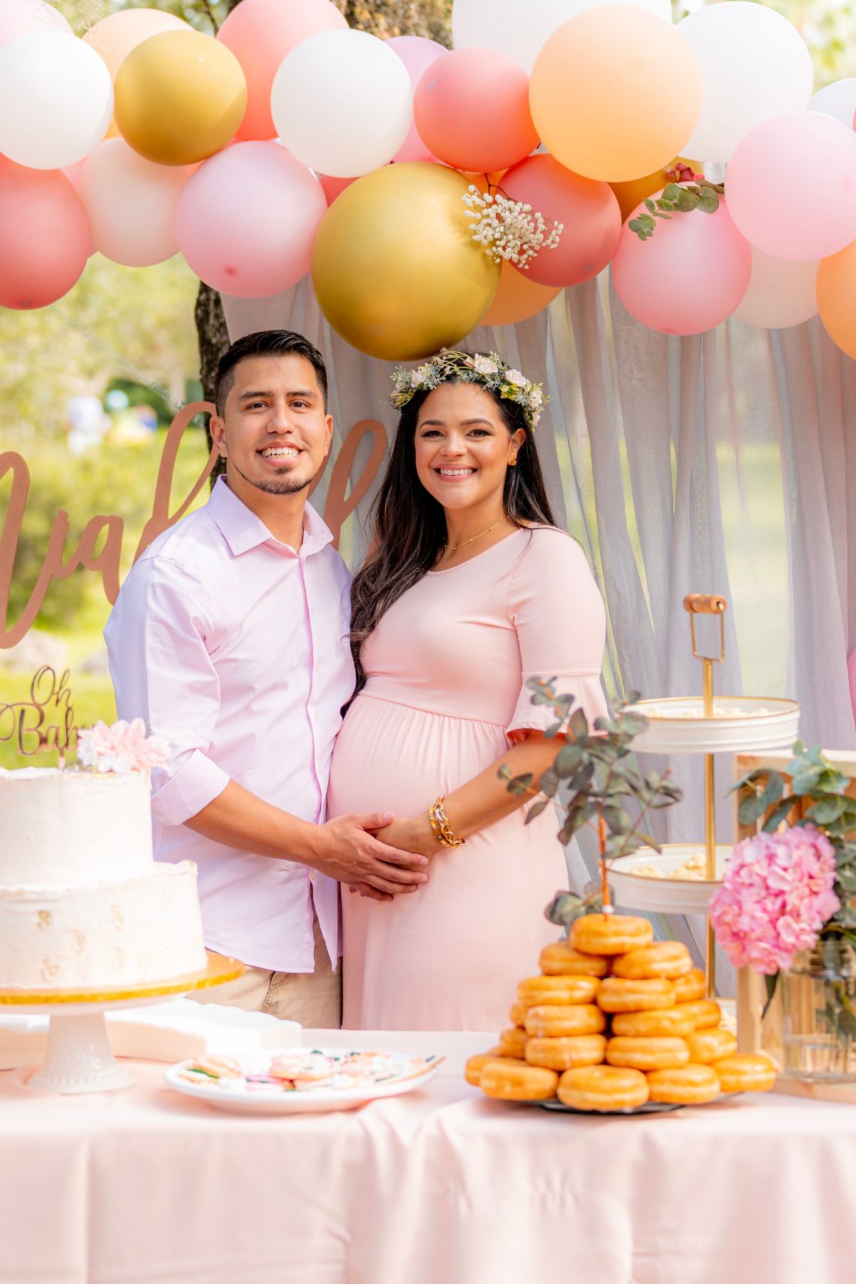 A couple wearing pink poses in front of pink and gold balloons at a baby shower.