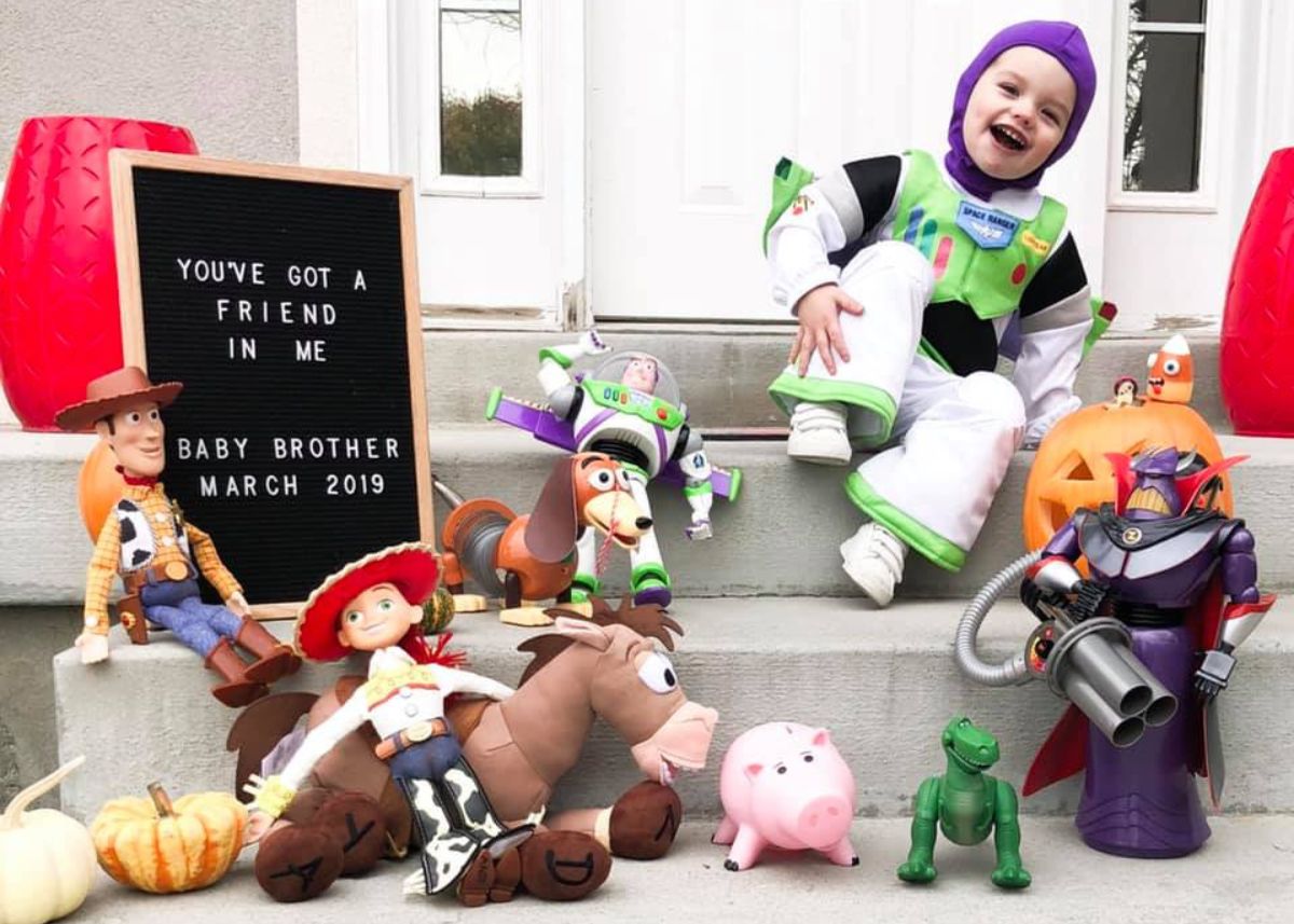 Boy in Buzz Lightyear costume surrounded boy Toy Story toys and a sign that says brother on the way.
