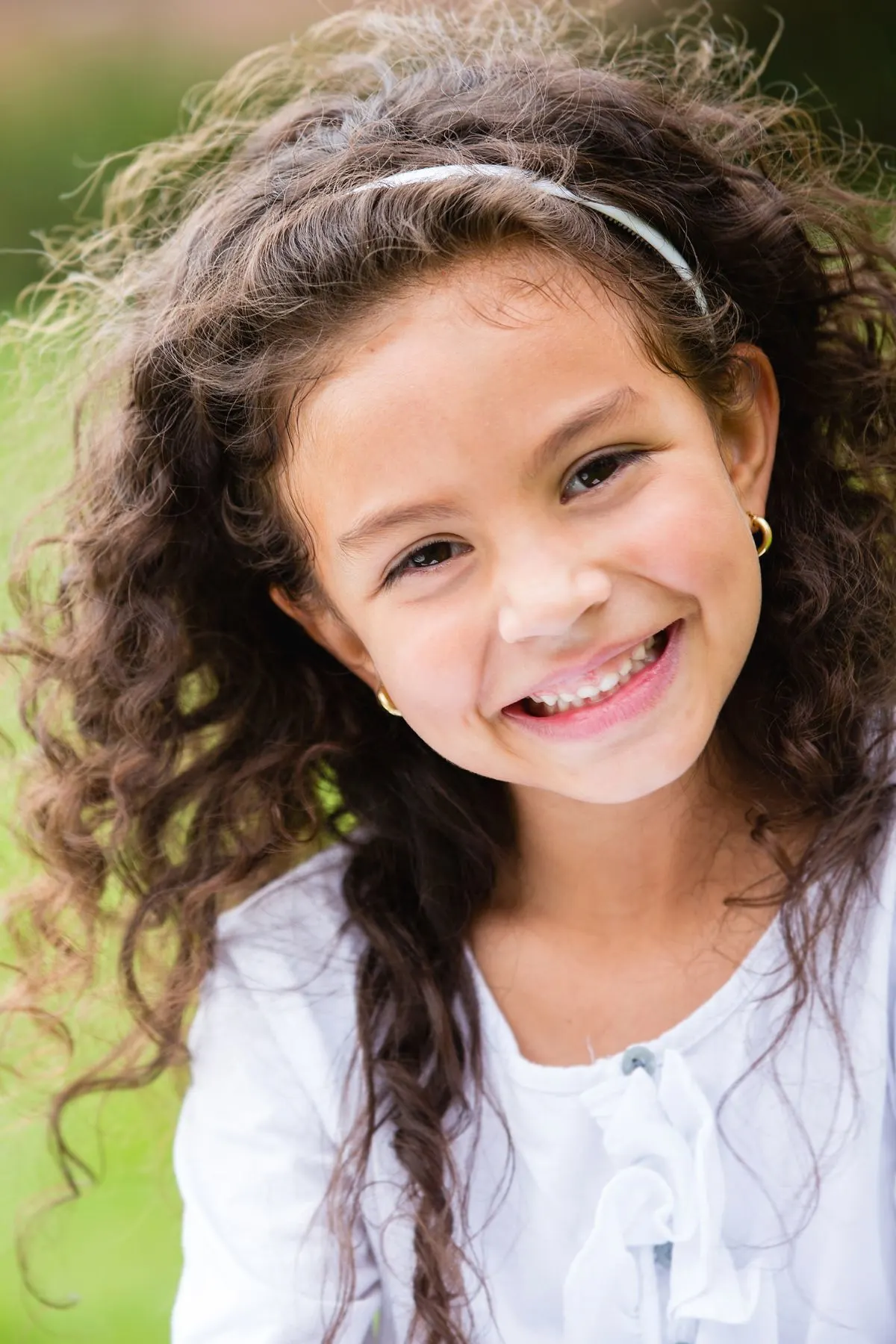 Smiling girl with big curly hair and white headband standing outside.