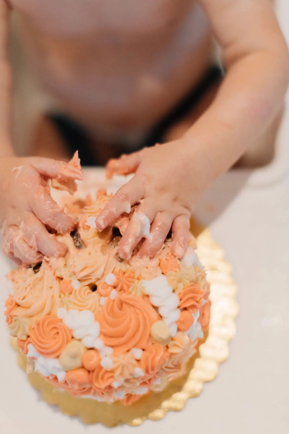 Baby plays in white, pink, and tan frosting on smash cake.