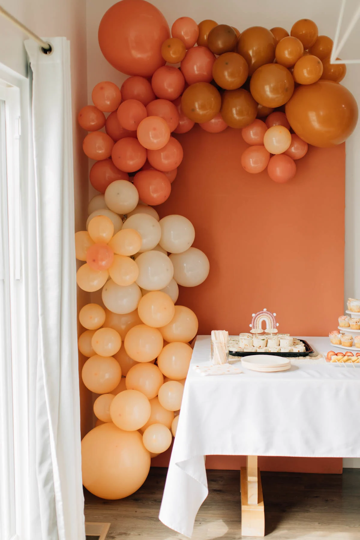 Boho colored balloon garland on rust colored arch behind food table.