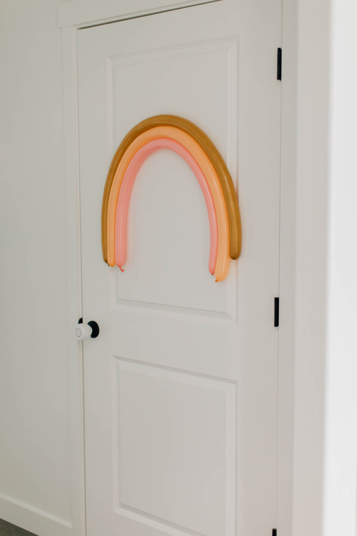 Tan and pink balloon rainbow on white door.