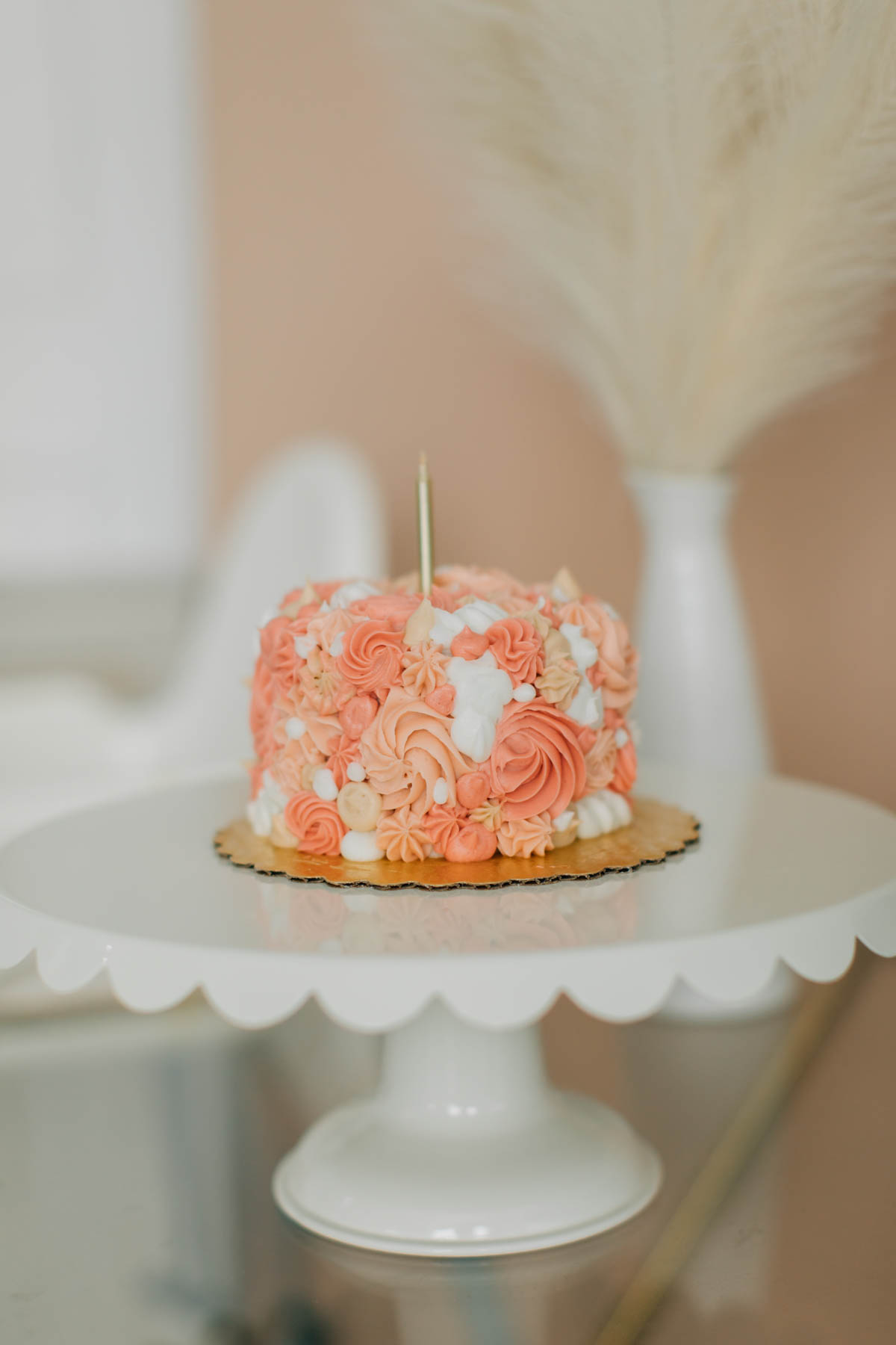 Boho smash cake with white, tan, and pink frosting swirls on white cake stand.