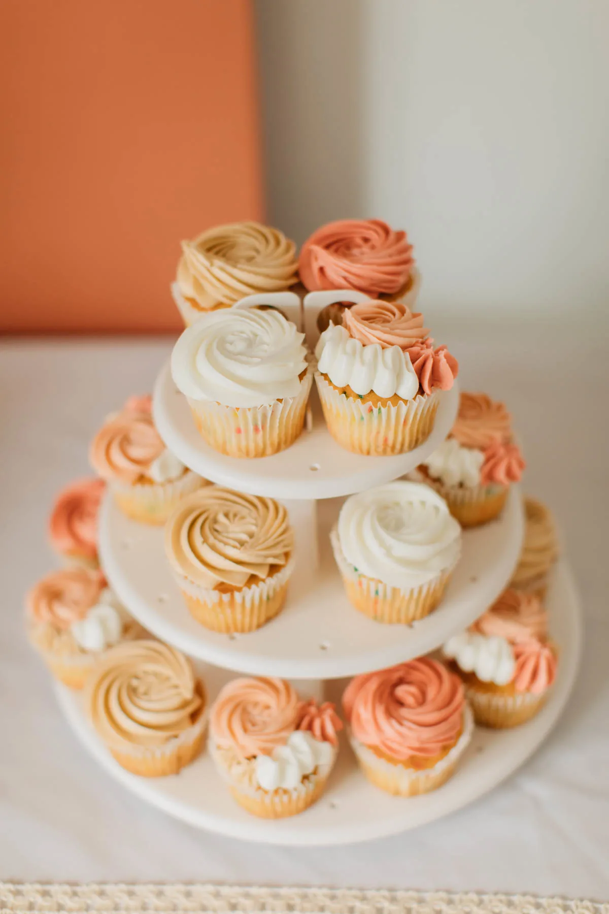 Cupcakes with pink, tan, and white frosting on white cupcake stand.