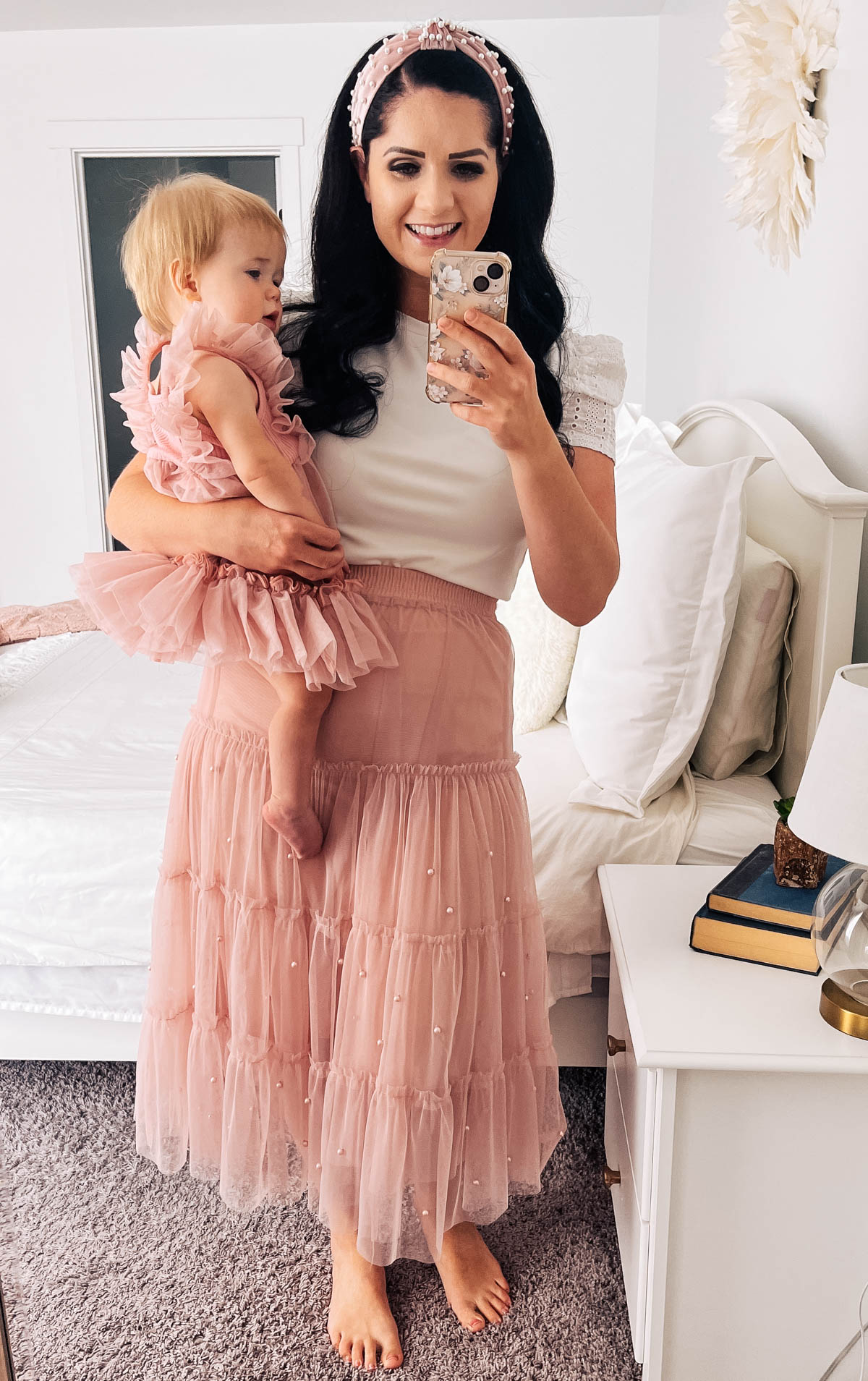 Mom wearing pink tulle skirt takes mirror picture with baby girl wearing pink dress.