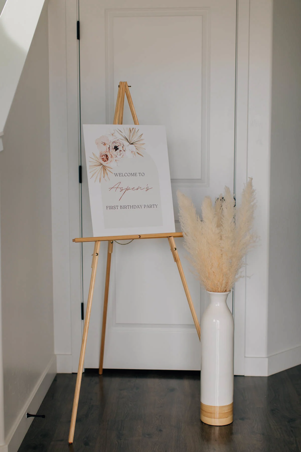 Party sign on wood easel next to floor vase with pampas grass.