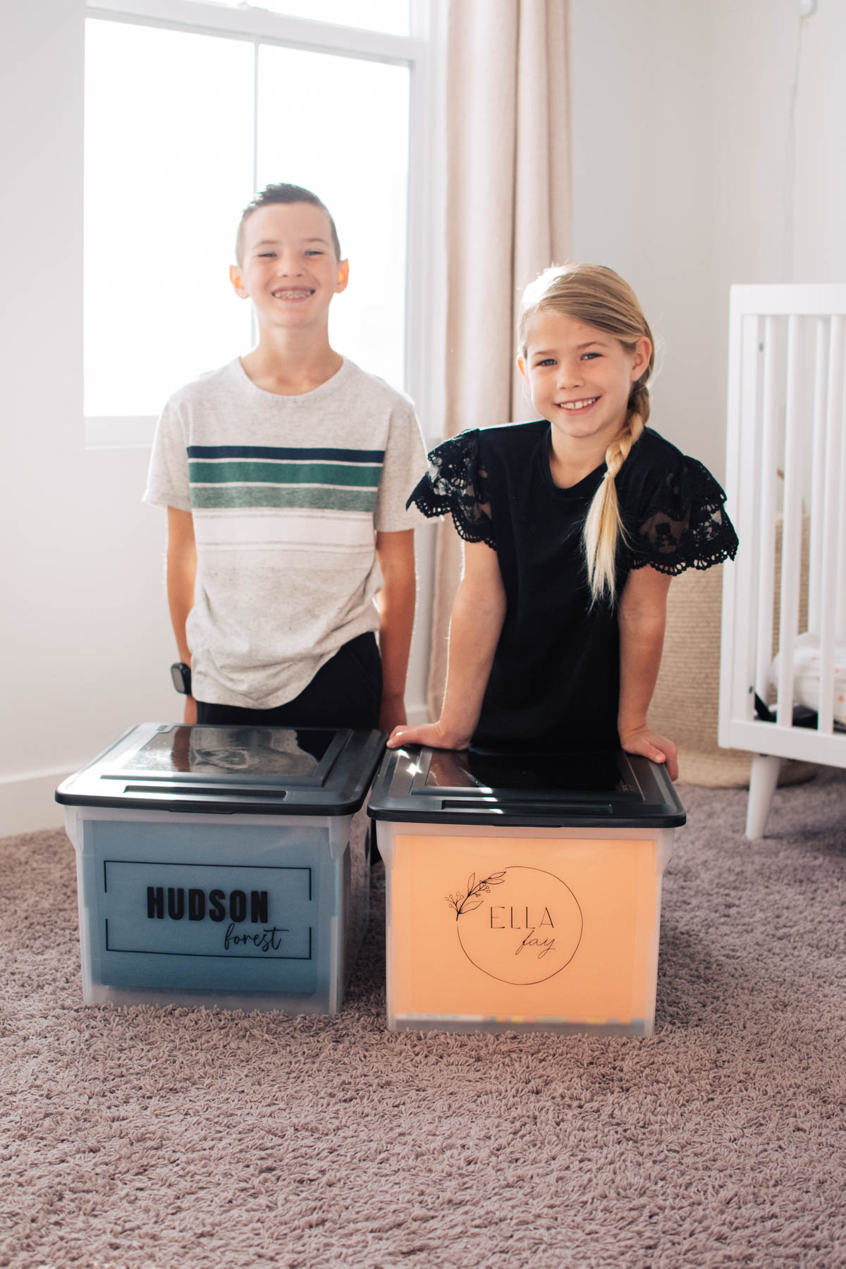 Two children smile while sitting behind their memory box personalized with their name.