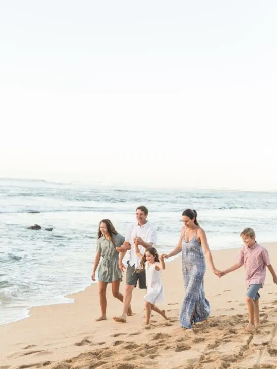 A family walks hand in hand in coordinating outfits on a beach by the shore.
