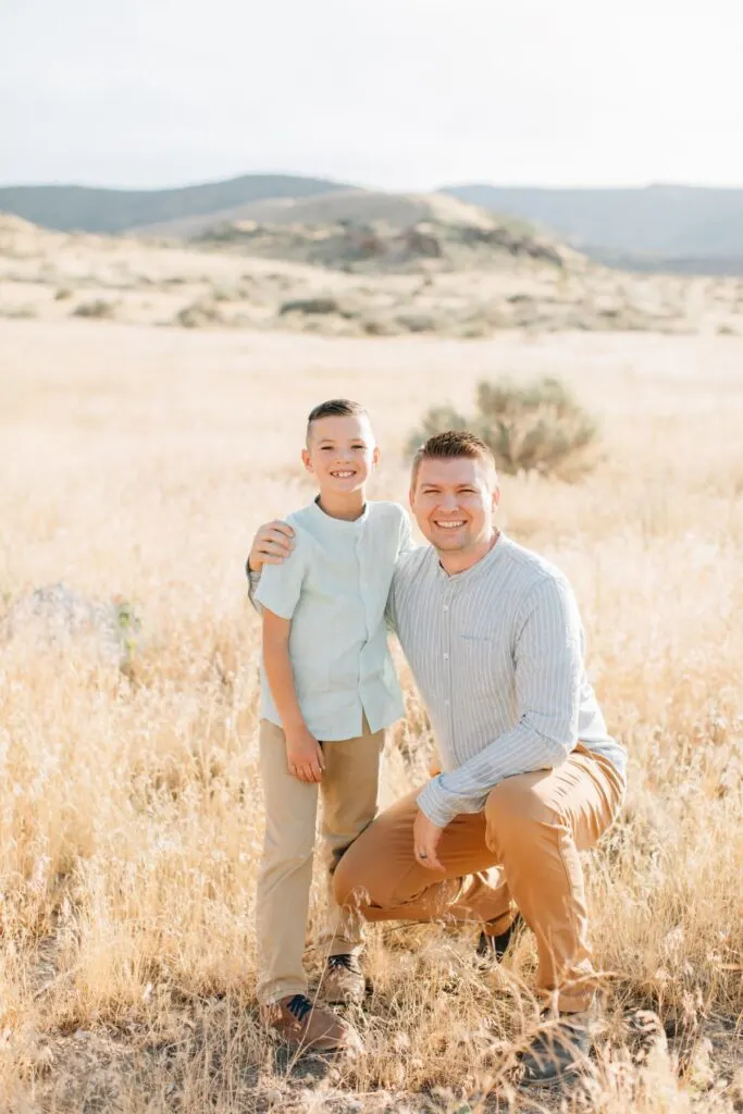 Father and son wearing green shirts pose in field of tall tan grass.