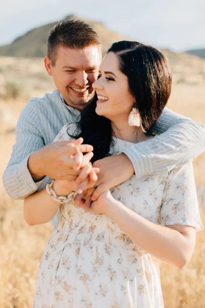 Husband wraps arms around wife while they smile and laugh.