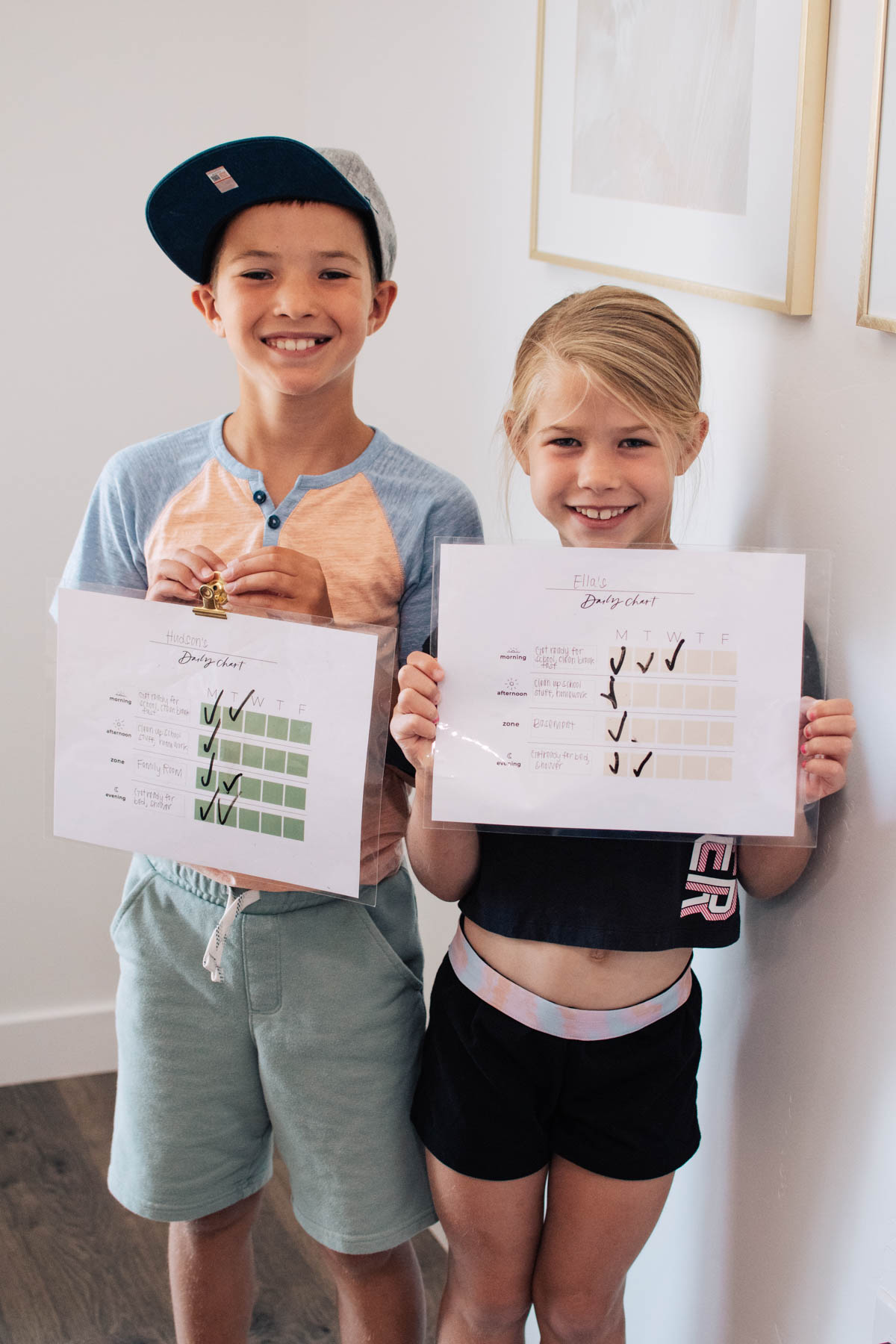 Boy and girl smile and hold up laminated daily charts with some check marks. 
