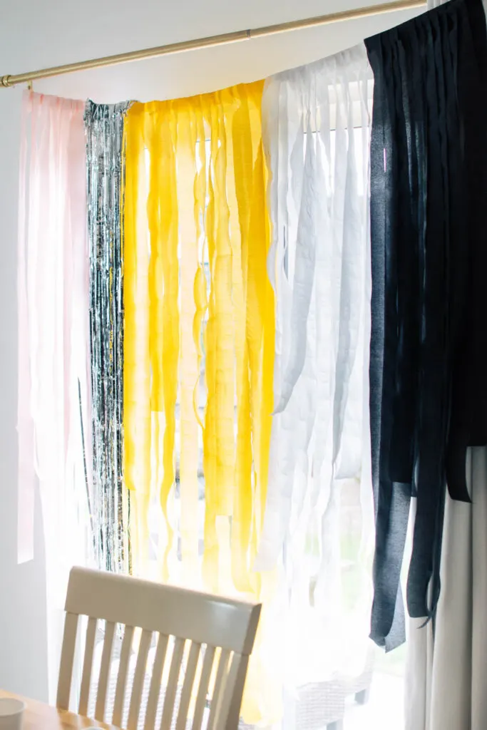 Back to school backdrop with pink, silver, yellow, white, and black streamers hangs from curtain rod.