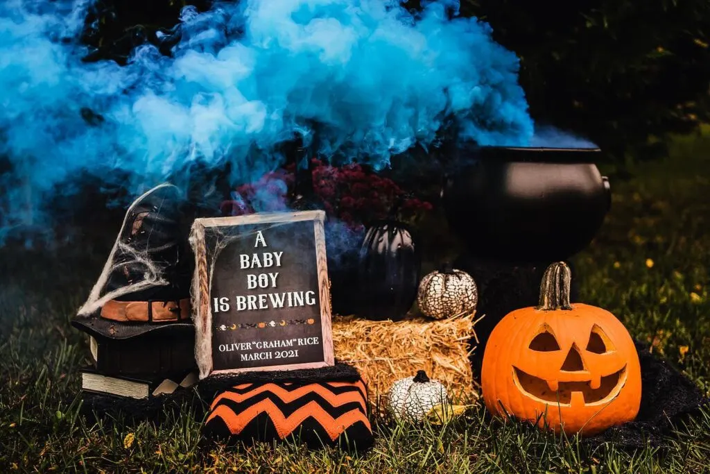 A sign that reads "A Baby Boy is Brewing" next to a cauldron with blue smoke and Halloween decorations.