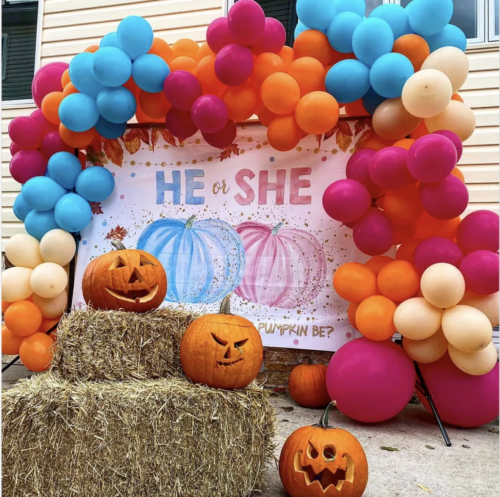 Gender reveal balloon garland placed over pumpkin backdrop that says "he or she."