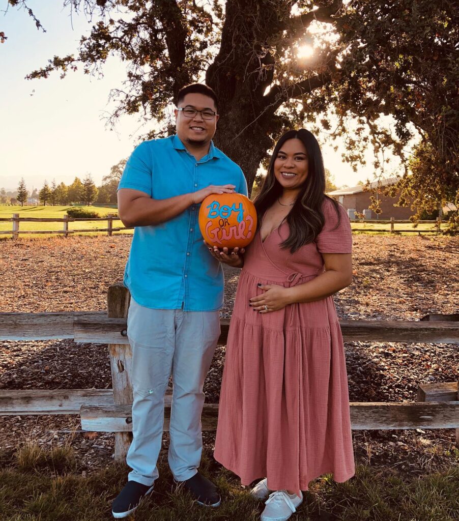 A couple dressed in blue and pink holds a gender reveal pumpkin.