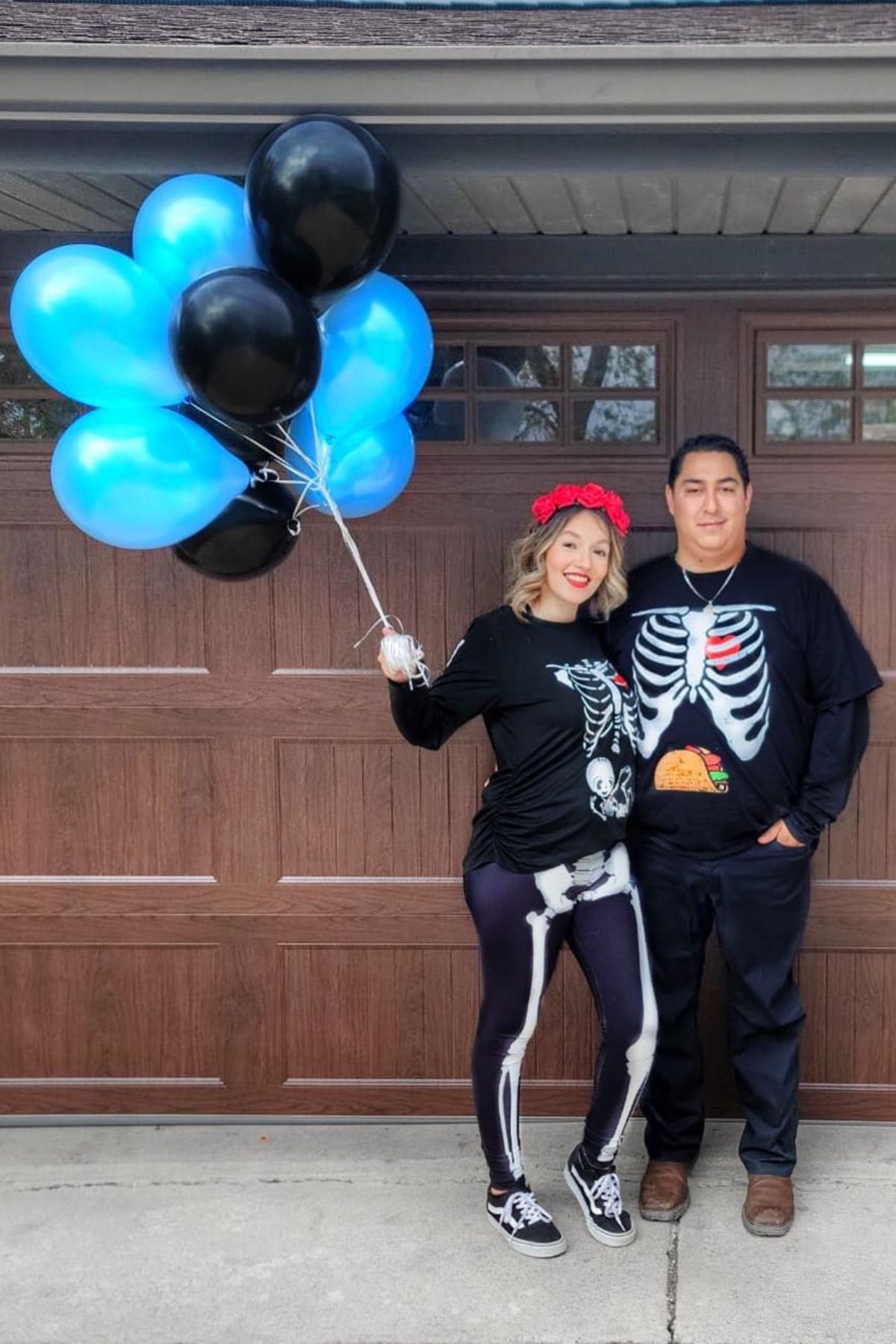 A couple dressed in skeleton costumes holding blue and black balloons.