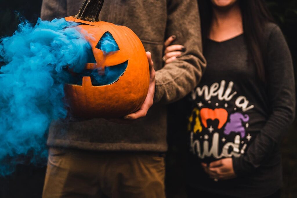 A couple holds a jack-o-lantern pumpkin with blue smoke coming out of the holes.