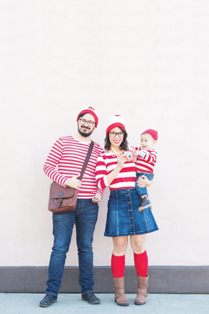 Man and woman dressed as Where's Waldo hold baby boy with matching costume.