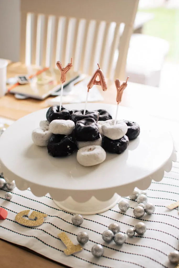 Powdered sugar and chocolate donuts on white cake stand with yay candles.