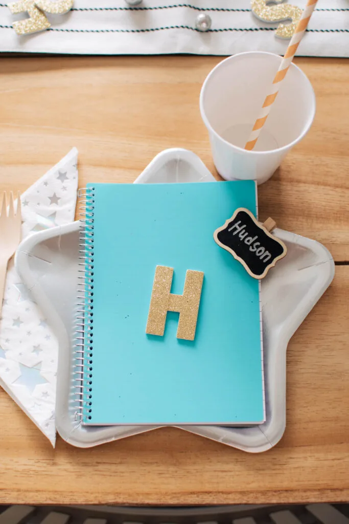Blue notebook with gold letter H and chalkboard clip on silver star plate.