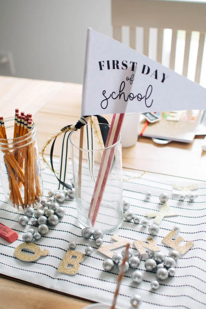 First day of school pennant with ribbons and pencils in glass jars on table runner.