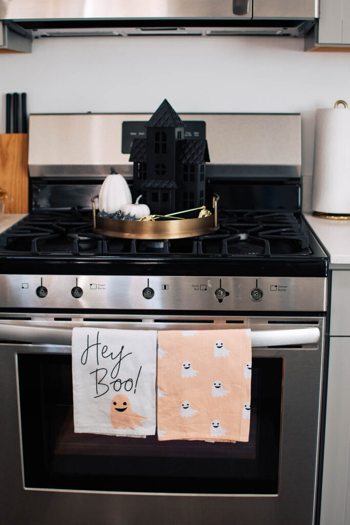 Gold tray with Halloween decorations on stove top and pink towels hanging from kitchen stove handle.