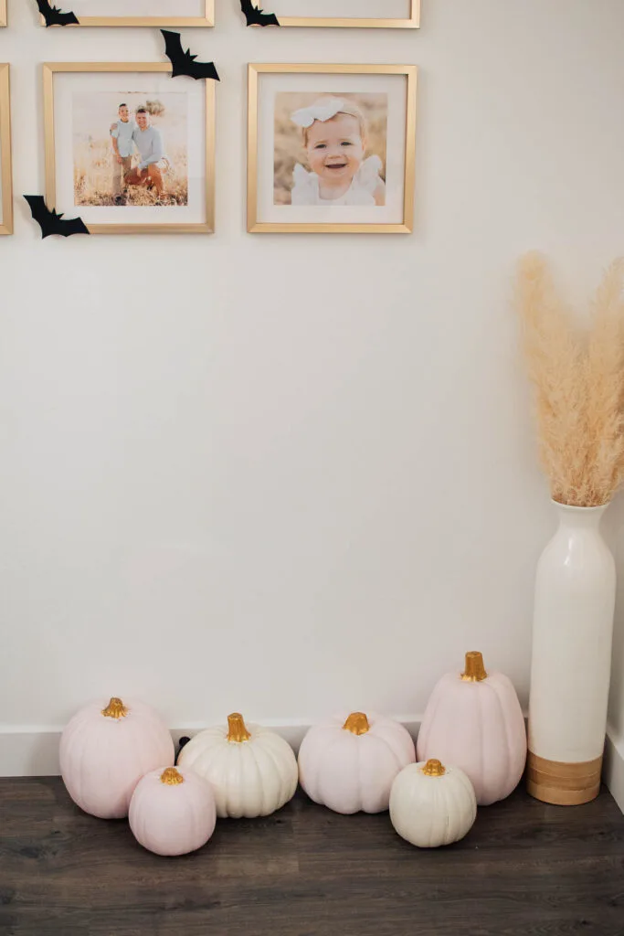 Pink painted pumpkins on floor next to pampas grass arrangement and frames with bats on them.