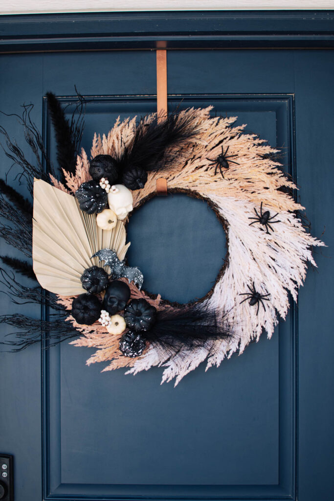 Boho Halloween wreath with pampas grass, skeletons, and pumpkins hangs on navy door.