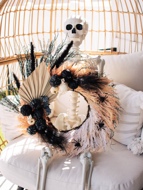 Skeleton decoration holds Halloween wreath with black embellishments.