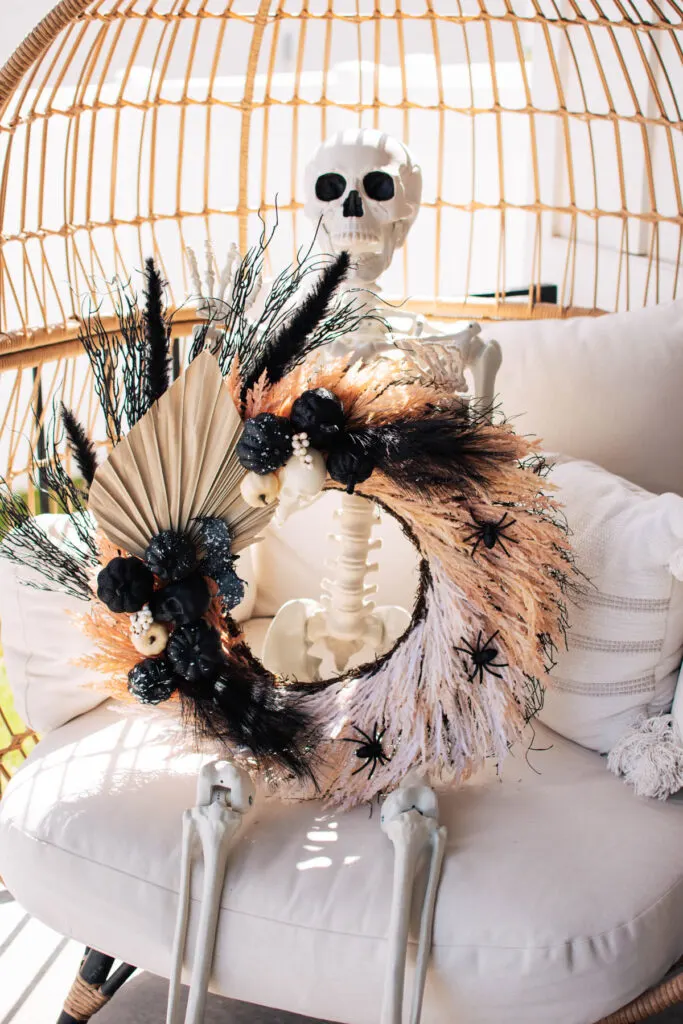 Skeleton decoration holds Halloween wreath with black embellishments.