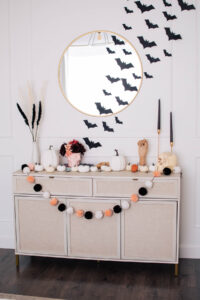 Console table with pink, cream, and black Halloween decorations including black candles and skulls.