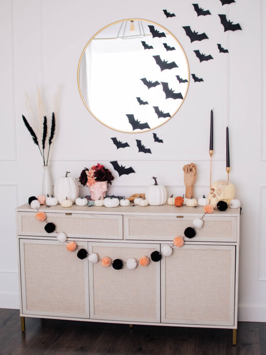 Console table with pink, cream, and black Halloween decorations including black candles and skulls.