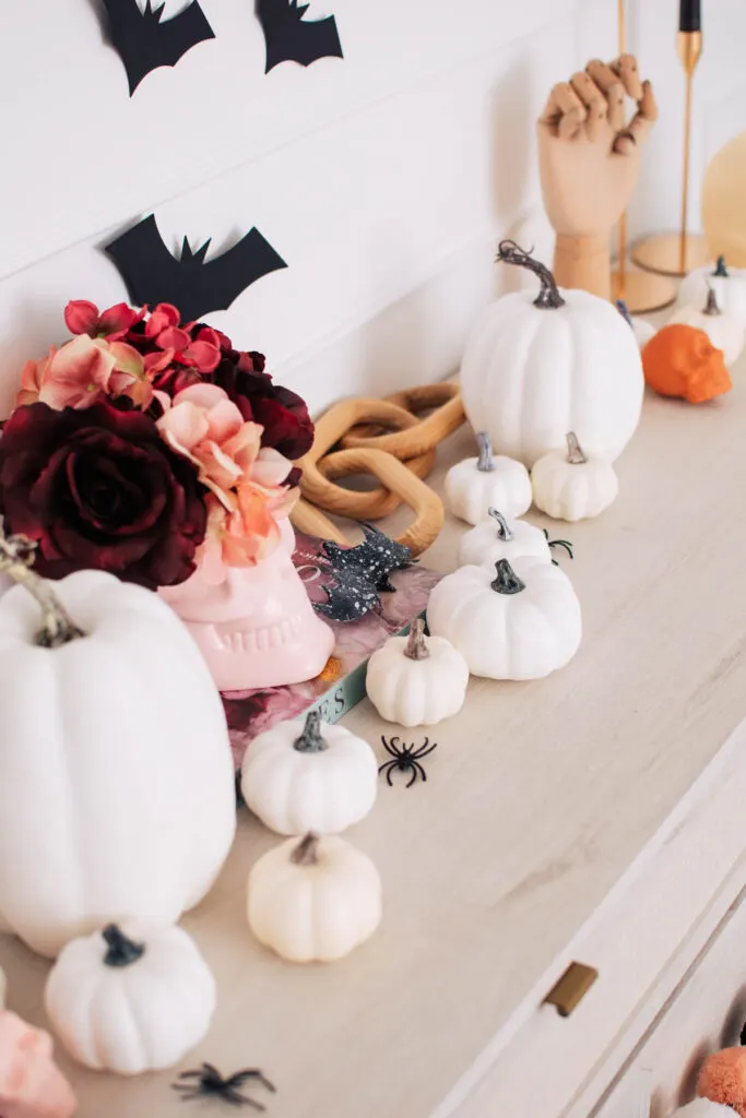 Various size white plastic pumpkins, pink skull vase and spiders on console table.