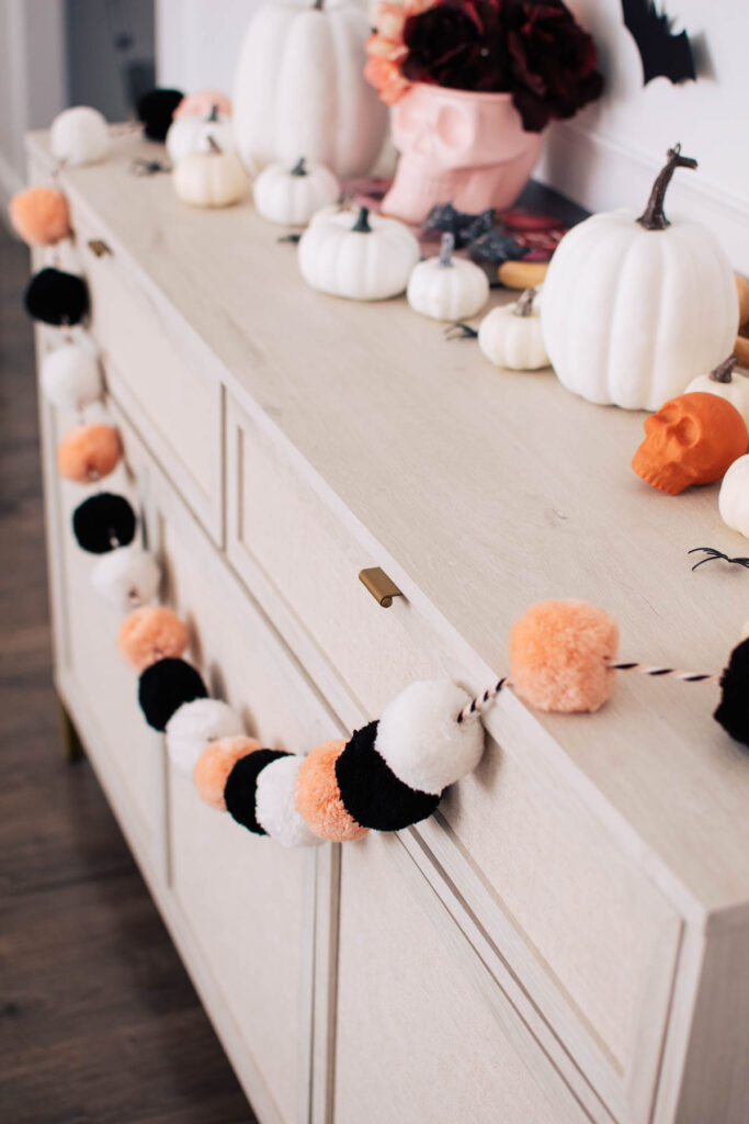 Black, pink, and white pom pom garland hangs from front of beige console table.