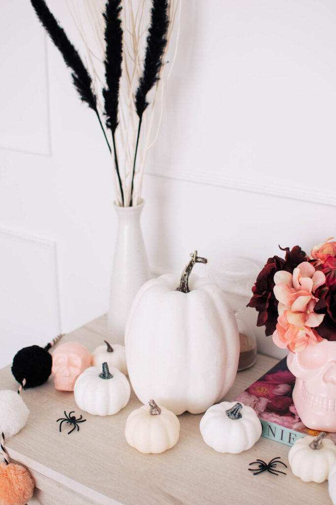 White plastic pumpkins in front of cream vase full of white branches and black pampas grass.