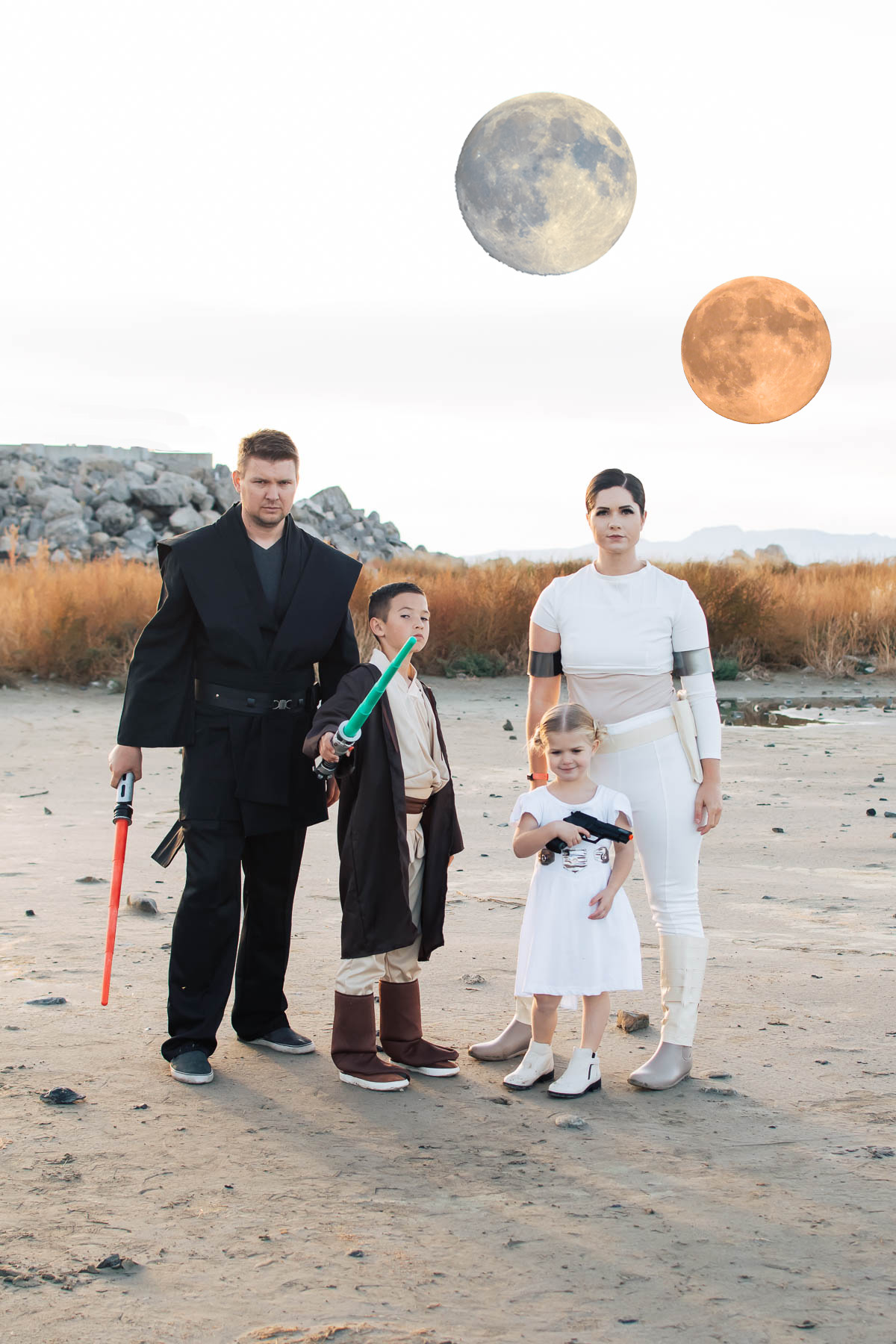Family of 4 dressed as Star Wars characters poses on sandy beach with fake moons in the background.