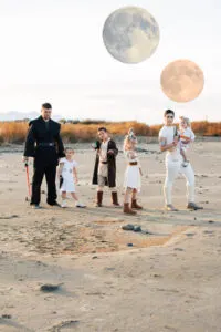 Family of 6 dressed in Star Wars costumes poses on sandy terrain with fake moons in the background.