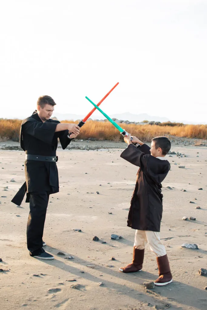 Man wearing black costume and boy wearing Luke Skywalker costume fight with light sabers.