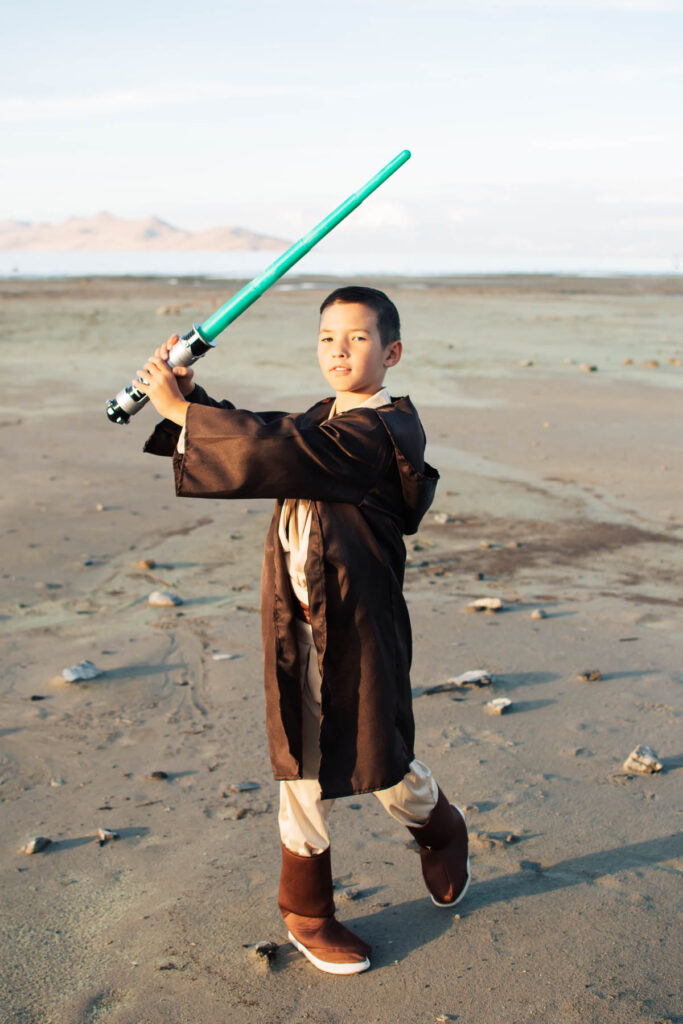 Boy wearing Luke Skywalker costume holds green light saber in air.
